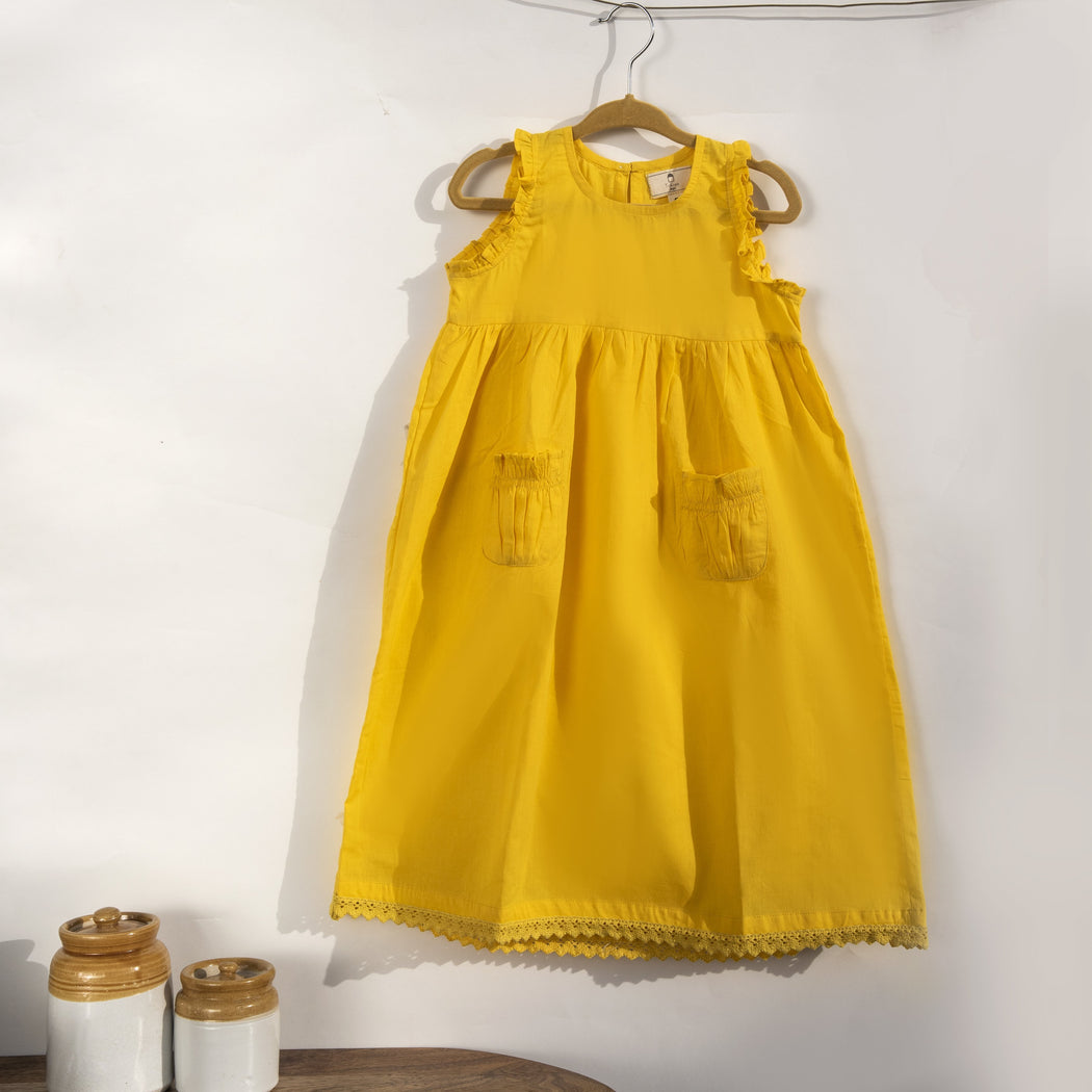 A sunshine yellow colored sleeveless dress for kids in cotton mulmul. This mid length dress has front pockets and a back button fastenings, accentuated with ruffles on the sleeve, neck and pockets.